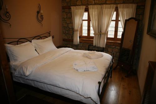 a bedroom with a bed with white sheets and two windows at Roes Suites in Kato Loutraki