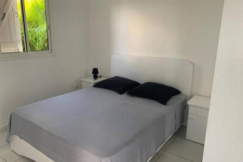 een wit bed met twee zwarte kussens in een slaapkamer bij Gîtes de Corneille, Bungalow Sweet Mango in Le Moule