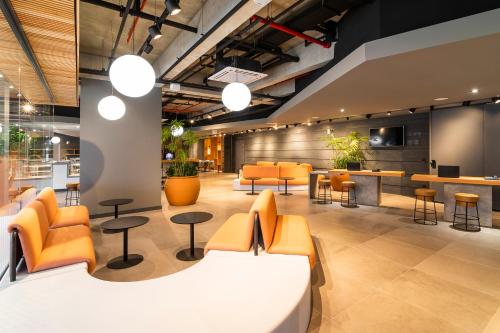 a lobby with orange chairs and tables and a bar at Novotel Criciuma in Criciúma