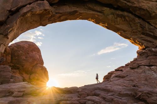 a person standing in front of a cave with the sun in the background at Under Canvas Moab in Moab
