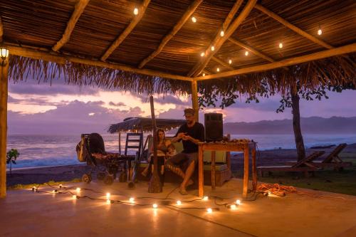 a man and a child sitting under an umbrella on the beach at Beach Break Hotel & Surf Camp de Playa Venao in Playa Venao