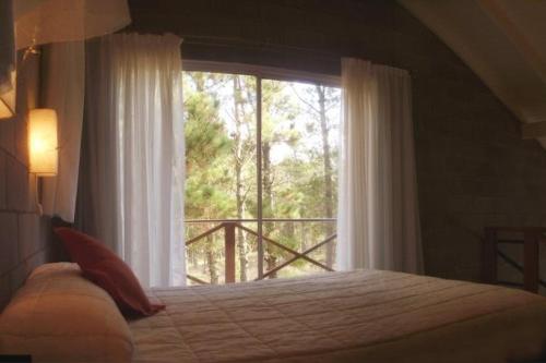 um quarto com uma cama e uma grande janela em Loft Hadas del Bosque em Mar de las Pampas