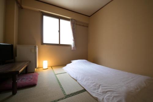 a bedroom with a white bed and a window at Heiwadai Hotel Arato in Fukuoka