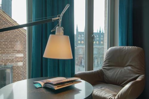 a desk with a lamp and a chair and a table with books at Motel One Lübeck in Lübeck