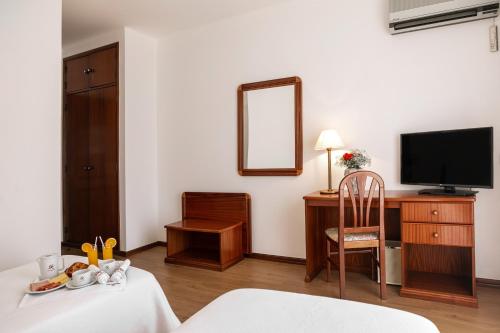a room with a bed and a desk with a television at Hotel Comendador in Bombarral
