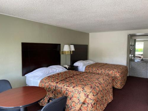 two beds in a hotel room with a table and chairs at Red Carpet Inn Greensboro in Greensboro