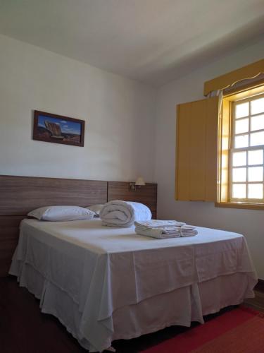 a bedroom with a bed with white sheets and a window at Pousada o Amanhecer in Tiradentes