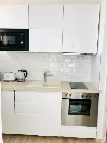 a kitchen with white cabinets and a sink and a stove at Belvárosi Stúdió Apartman in Kecskemét