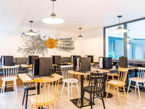 a restaurant with wooden tables and chairs andwindows at ibis Styles Rouen Val De Reuil in Val de Reuil