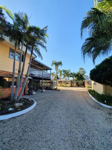 a gravel driveway with palm trees in front of a building at Park Beach Cabins in Coffs Harbour