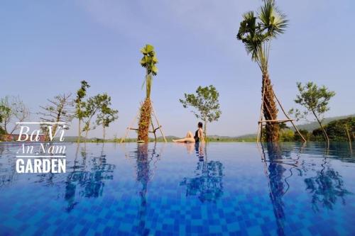 un homme assis au milieu d'une piscine d'eau bordée de palmiers dans l'établissement Bavi Annam Garden, à Ba Vì