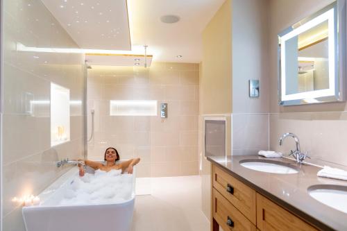 a woman is in a bath tub in a bathroom at Carden Park Hotel, Golf Resort and Spa in Tilston