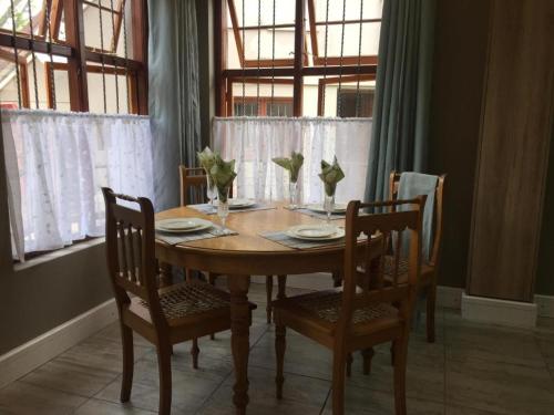 Rozenhof Guest Cottages في جورج: طاولة طعام مع أربعة كراسي وطاولة خشبية مع لوحات و مزهريات