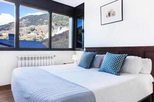 a white bed with blue pillows in a room with windows at Vista Tarter Apartments in El Tarter