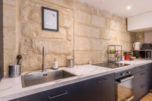 une cuisine avec un évier et un mur en pierre dans l'établissement La Parenthèse Roucher Montpellier - Duplex Climatisé T2 Cœur écusson MEUBLE TOURSIME 3 ETOILES, à Montpellier