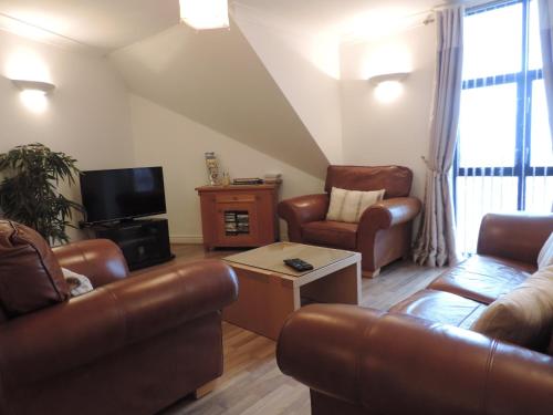 a living room with leather furniture and a tv at Sea Breeze Apartment in St Austell