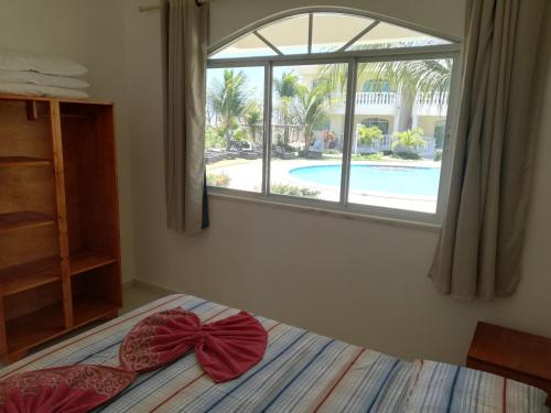 a bedroom with a bed and a window and a pool at Apartamento 150m da praia de Canoa Quebrada in Canoa Quebrada