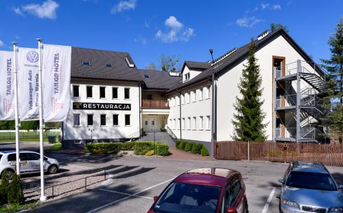 a white building with cars parked in a parking lot at Tailor Hotel Sport & Conference in Morąg