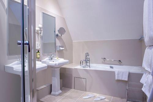 een witte badkamer met 2 wastafels, een bad en een spiegel bij Chateau De Montreuil in Montreuil-sur-Mer