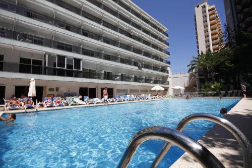 einen Swimmingpool mit Leuten, die in einem Gebäude auf Stühlen sitzen in der Unterkunft Hotel Perla in Benidorm