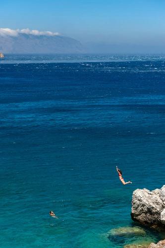 two people swimming in the ocean near a large rock at Pagali Hotel in Órmos Aiyialís