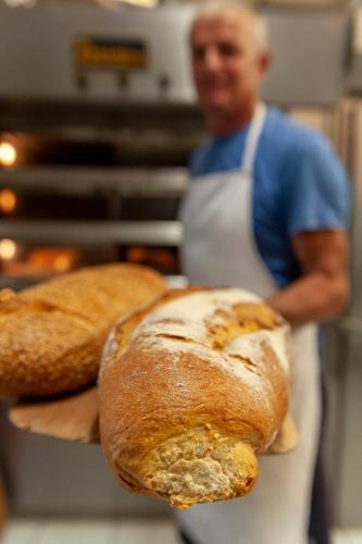a man in a kitchen holding two loaves of bread at Pagali Hotel in Órmos Aiyialís