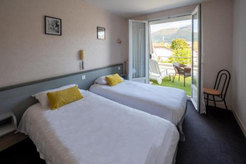 two beds in a hotel room with a balcony at Hôtel du Soleil Levant in Argelès-Gazost