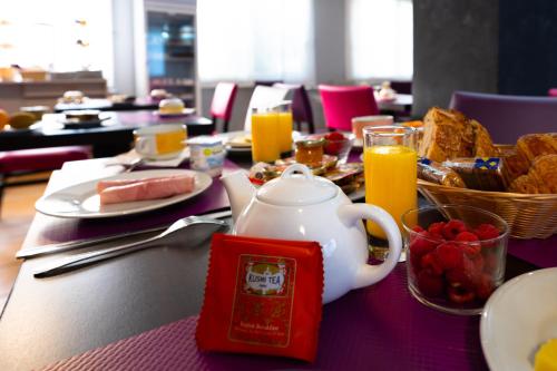 a table with a tea pot and breakfast foods and orange juice at Hôtel du Soleil Levant in Argelès-Gazost