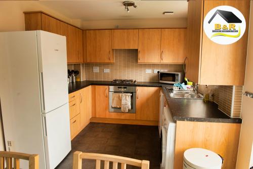 a kitchen with wooden cabinets and a white refrigerator at B and R Serviced Accommodation Amesbury, 3 Bedroom House with Free Parking, Super Fast Wi-Fi 145Mbs and 4K smart TV, Archer House in Amesbury
