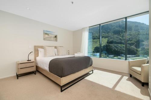 a bedroom with a bed and a chair and a large window at Oceanside Haven Resort with Luxury Sea Views in Mount Maunganui