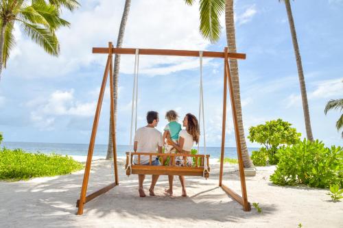 a group of people sitting on a swing on a beach at Reethi Faru Resort - Stay 5 Nights or more & Enjoy a Free Sunset Cruise in Raa Atoll