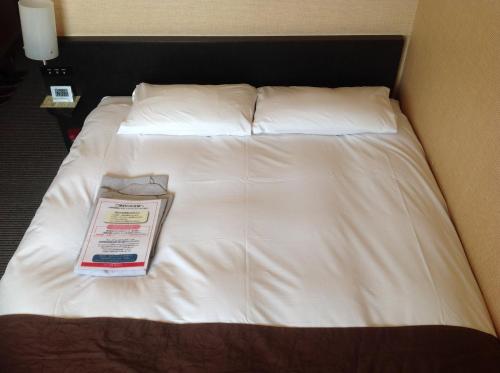 a bed with white sheets and a box on it at Hotel Crown Hills Kokura in Kitakyushu