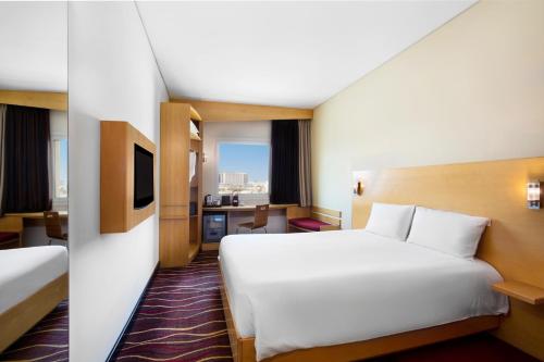 Habitación de hotel con cama blanca grande y escritorio. en ibis Muscat, en Mascate