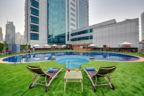 a swimming pool with two chairs and a table in the grass at Sunday Marina View Hotel Apartments in Dubai