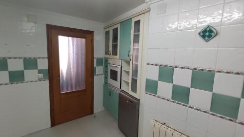 una cocina con paredes de azulejos verdes y blancos y una puerta en Ca la Glori, en Los Corrales