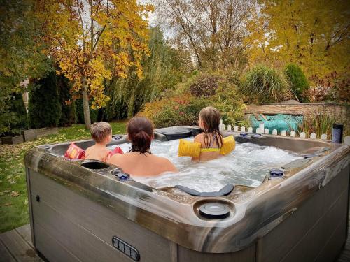 3 personnes dans un jacuzzi dans un jardin dans l'établissement Villa 200m2 avec PISCINE chauffée & SPA & sauna & kota-grill, à Laval-sur-Vologne
