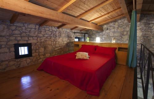 1 dormitorio con 1 cama roja en una pared de piedra en Trullo in the Wood, en Nardò