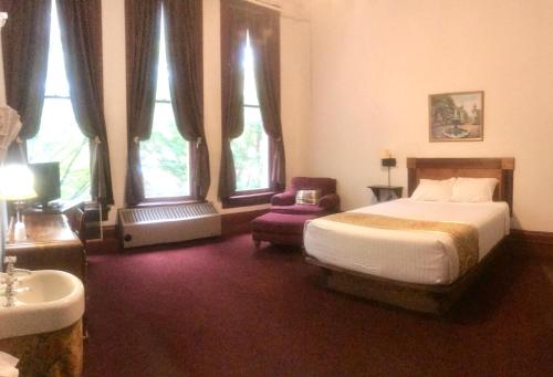 a bedroom with a bed and a chair and windows at The Monarch Hotel in Port Townsend