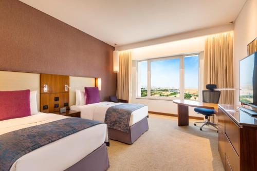 a hotel room with two beds and a desk and a window at Crowne Plaza Muscat OCEC, an IHG Hotel in Muscat