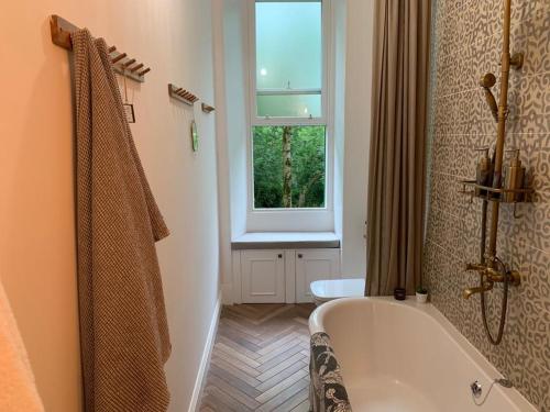 La salle de bains est pourvue d'une baignoire et d'une fenêtre. dans l'établissement Oakshaw Apartment, à Paisley