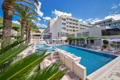 a swimming pool with palm trees in front of a building at Mediteran Hotel & Resort in Budva