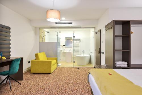 a hotel room with a bed and a yellow chair and a tub at Charm Boutique Hotel in Satu Mare