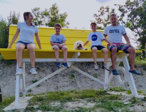 a group of people sitting on a yellow bench with a dog at Madama Langa Country House con piscina nelle vigne in Montelupo Albese