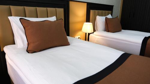 two beds in a hotel room with white sheets and brown pillows at Dimen Hotel in Bursa