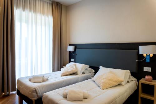 two beds in a hotel room with a window at Hotel Victoria in Cuneo
