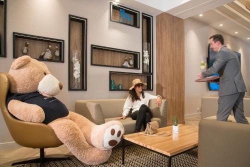 a man and woman sitting in a living room with a giant teddy bear at Novotel Nice Arenas Aeroport in Nice