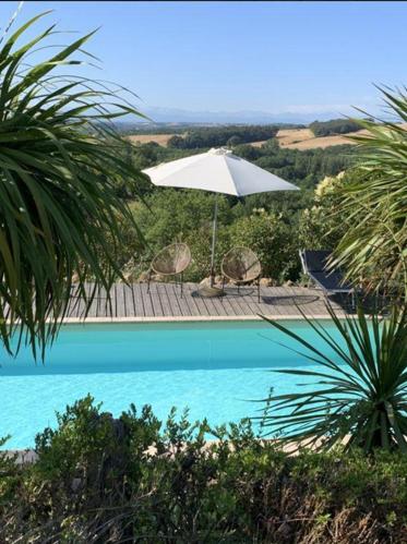 a white umbrella and chairs and a swimming pool at L'Apouticayre in Montaut