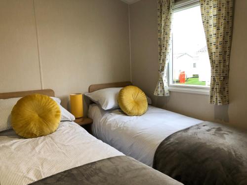 2 camas con almohadas amarillas en una habitación con ventana en Whitley bay 4 berth Luxury Caravan, en Newcastle