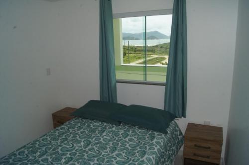 um quarto com uma cama e uma grande janela em Residencial Esmeralda-Vista ao Mar em Palhoça