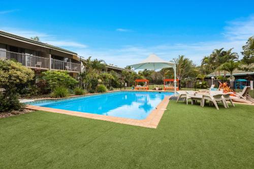 a pool with a table and chairs next to a building at Ballina Beach Resort in Ballina